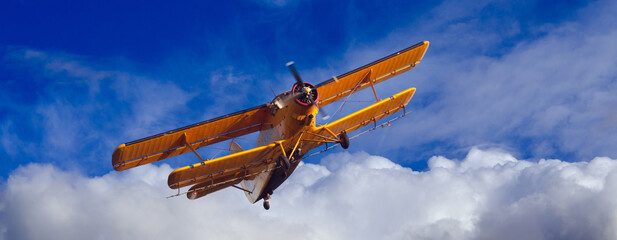 Agricultural airplane spraying pesticides on agricultural fields in summer against blue sky and white clouds