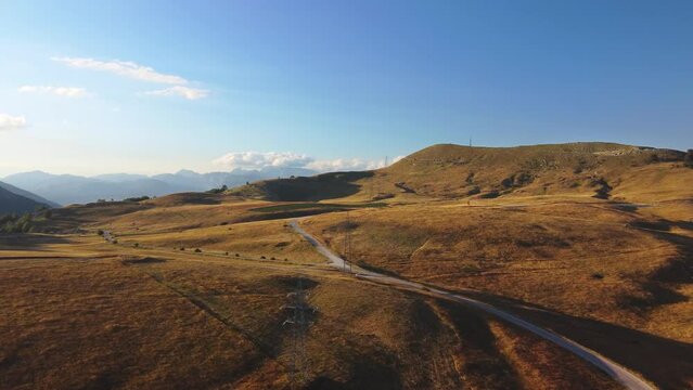 Panoramic aerial drone view breathtaking landscape. Top air view of hills and a empty road bathed in sunset light with high mountain peaks in the background. Beauty of nature