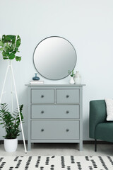 Chest of drawers and stylish round mirror on white wall indoors. Interior design