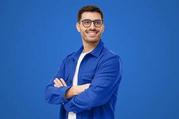 Confident young man in casual blue shirt looking away, standing with crossed arms