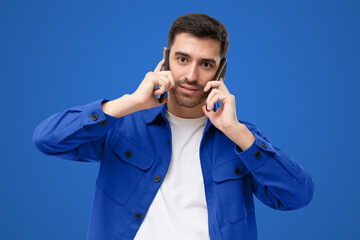 Overwhelmed business man talking on two phones, isolated on blue background