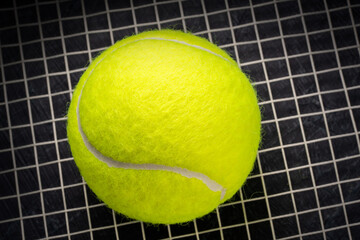 Tennis ball isolated on tennis racquet background, Yellow Tennis ball sports equipment on black background.