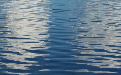 Calm blue water surface with sky reflection as a background