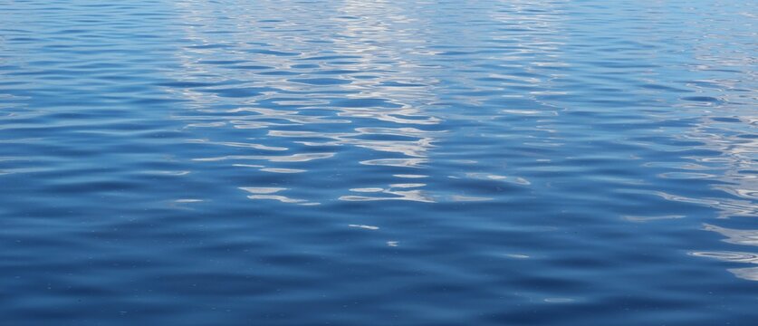 Panoramic view on calm glossy light blue water texture as background