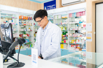 Medical pharmacy and healthcare providers concept. Handsome Asian man pharmacist working inspection medical product, drugs, medicine and supplements in package at cashier counter in modern drugstore.