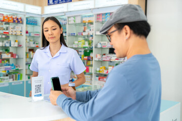 Obraz premium Medical pharmacy and contactless payment concept. Asian man patient customer using mobile phone scan QR code on counter making online banking payment buying medicine, drugs and supplement in drugstore