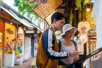 Fototapeta na wymiar Young Asian couple enjoy and fun outdoor lifestyle shopping together at street market on summer holiday vacation. Happy man and woman choosing and buying fashion clothes together at clothing shop.