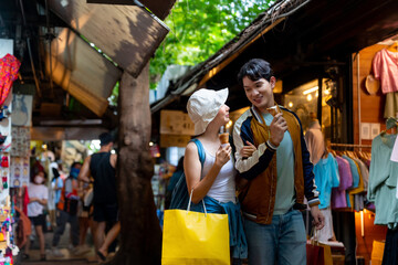 Young Asian couple enjoy and fun outdoor lifestyle shopping at street market on summer holiday vacation. Man and woman couple eating ice cream cone while walking and shopping at weekend street market.