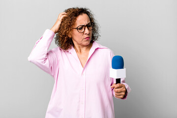 pretty middle age woman feeling puzzled and confused, scratching head. tv presenter with a...