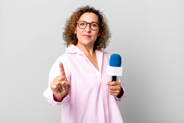 pretty middle age woman smiling proudly and confidently making number one. tv presenter with a...