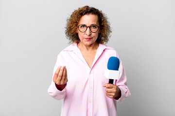 pretty middle age woman making capice or money gesture, telling you to pay. tv presenter with a...