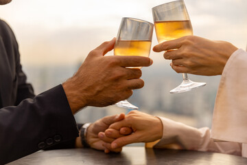 Caucasian couple celebrating at luxury skyscraper rooftop bar at summer sunset. Confident man and woman couple enjoy city lifestyle having dinner and cocktail drink at outdoor restaurant in evening.