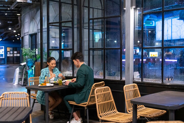 Asian couple celebrating holiday event at luxury restaurant bar in the city at night. Attractive man and woman enjoy city lifestyle shopping and having dinner with food and drink on travel vacation