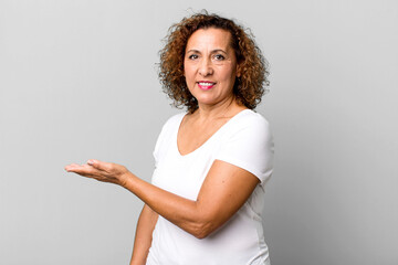 middle age hispanic woman smiling cheerfully, feeling happy and showing a concept in copy space...