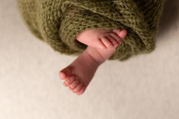 Newborn baby feet on an oatmeal background wrapped in a knitted blanket