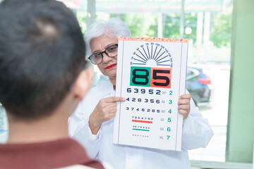 Middle-aged ophthalmologist examining young boy and giving eye consultation to Asian boy