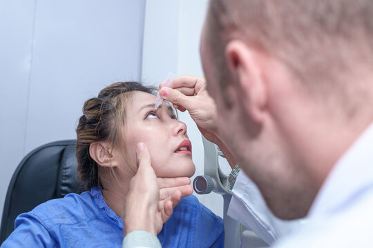 Male doctor ophthalmologists dripping eye drops on eyes of a female patient during a treatment at the ophthalmological office