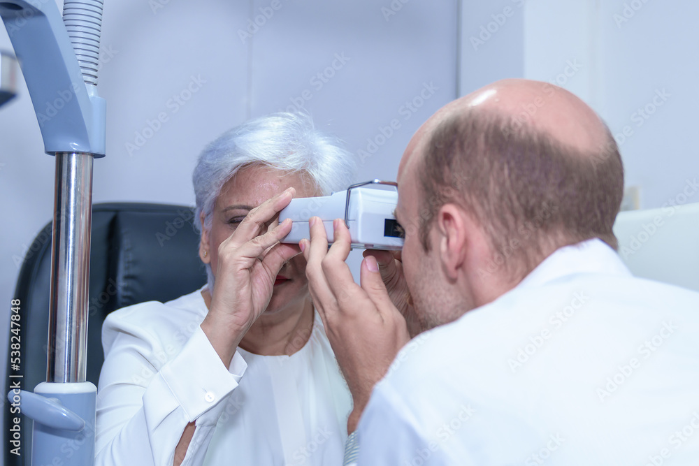 Wall mural Attractive male ophthalmologist is checking eye vision of middle aged woman in modern clinic, doctors and ophthalmology clinic patients.