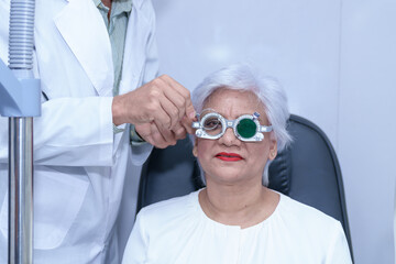 Attractive male ophthalmologist is checking eye vision of middle aged woman in modern clinic,...