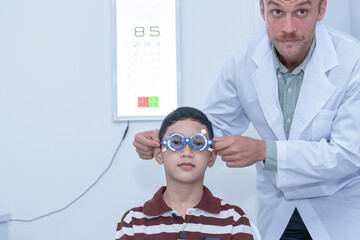 Smiling boy in glasses examining eyesight at a pediatric ophthalmologist  with grandma to support...