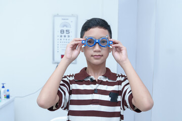 Smiling boy in glasses examining eyesight at a pediatric ophthalmologist  with grandma to support...
