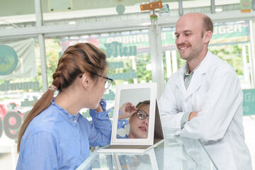 Fototapeta premium American man professional optician helping and selling young woman asia choosing spectacles glasses in optician store. used correct assist or defective eyesight.