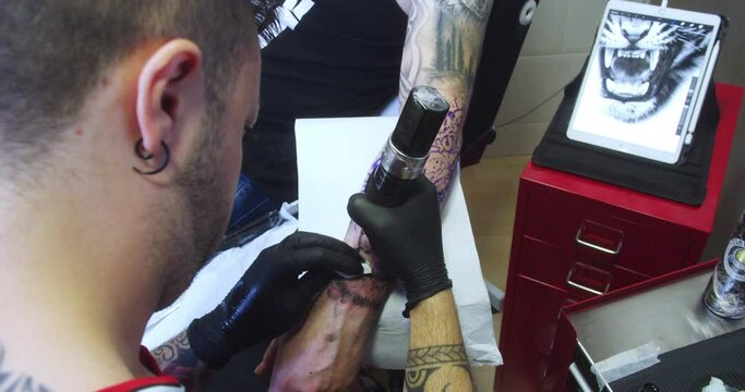 Professional tattoo artist tattoos and cleans a man's forearm.