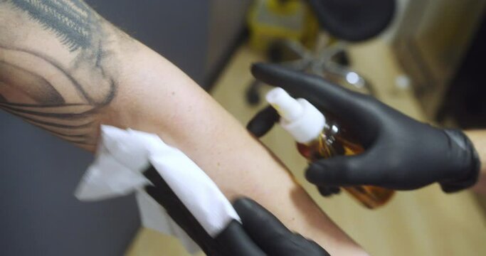 Professional tattoo artist cleans the forearm of the man who is going to be tattooed.