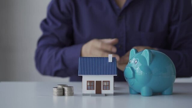 A young man puts a coin in a piggy bank for the purchase of a future house. Money Saving Ideas . 4k