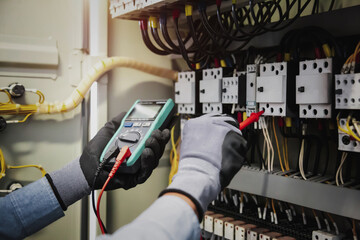 Electricity and electrical maintenance service, Engineer hand holding AC multimeter checking electric current voltage at circuit breaker terminal and cable wiring main power distribution board.