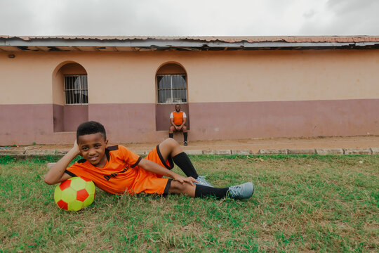 Child laying on grass while leaning on football with dad in the background