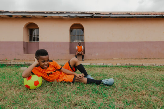 Little boy with soccer ball resting on grass and father watches in the background
