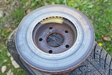 Bad grinded used ventilated brake rotor disc with abrasion stripes on winter tyre background
