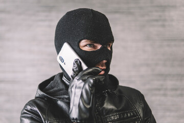 thief is talking on the phone in a black mask. The extortionist demands money for the kidnapping. a...