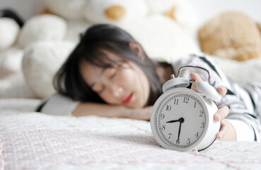 Young sleeping woman and alarm clock in bedroom at home,Woman in bed extending hand to alarm clock