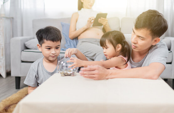 Asian Childrens Learning To Save Money, They Take Coins To Piggy Bank, They Feeling In Family Time