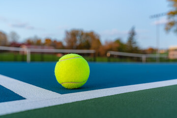 Photo taken in late evening under lights of a yellow tennis ball on blue tennis court with white...