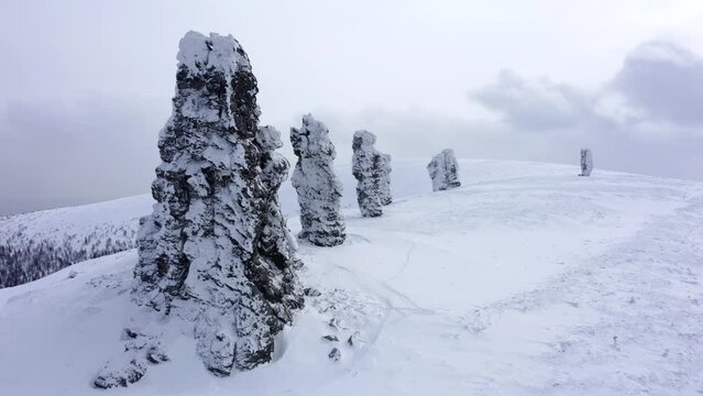 Flight on a copter in front of the snow-covered blocks of Manpupuner in winter. Aerial view on a drone Pillars of weathering (Mansi blockheads) in the snow - mountain Man-Pupu-ner "