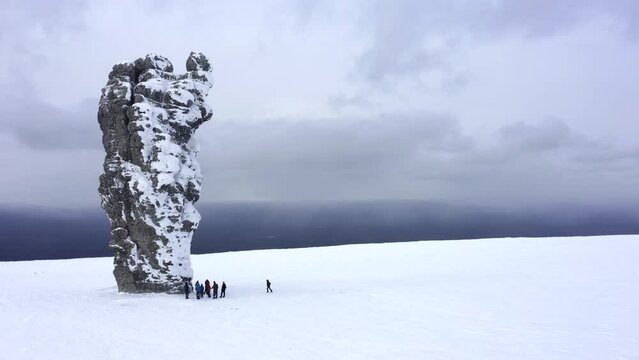 View from the copter a group of tourists near the snow-covered stone block Manpupuner in winter. Aerial view flying on a drone near the Pillars of weathering (Mansiysk blockheads) in the snow