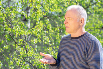 An elderly man with pills in his hand against the background of nature. Spring exacerbation of allergies