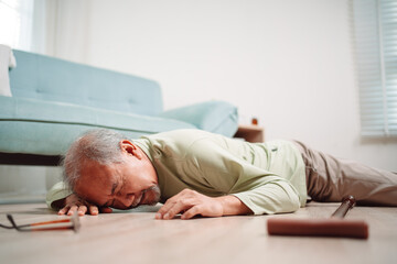 Obraz premium Asian senior man falling on the ground with walker in living room at home. Elderly older mature male having an accident heart attack for emergency help support from hospital. Insurance health care.