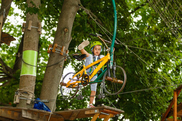 Little girl is standing on a rope, holding a rope with his hands. A child in a rope park passes obstacles