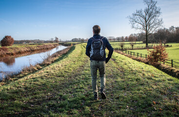 Male hiker with backpack walking alone on grass path in autumn season. 