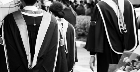 Black and white A group of male and female graduates wearing black robes outdoors on a rainy day in university concept graduating with a degree.