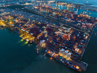 international shipping port load and unloading container by crane onto transport ships and trailer for import export distributing products to customers and consumer over lighting cityscape background