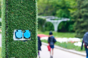 Electric sockets for charging on a pole with artificial green grass in the park