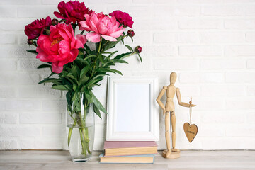 Purple peony flowers bouquet, books, frame and wooden dummy on the white brick wall background.