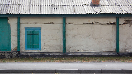 Fototapeta na wymiar White stone wall with a window with closed green shutters in the Kazakh city of Pavlodar. Banner with old wooden russian house. The concept of antiquity and decadence. A dilapidated abandoned building
