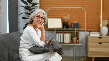 Fototapeta na wymiar Pleasant elderly woman browsing wireless internet on digital tablet, relaxing on couch at home