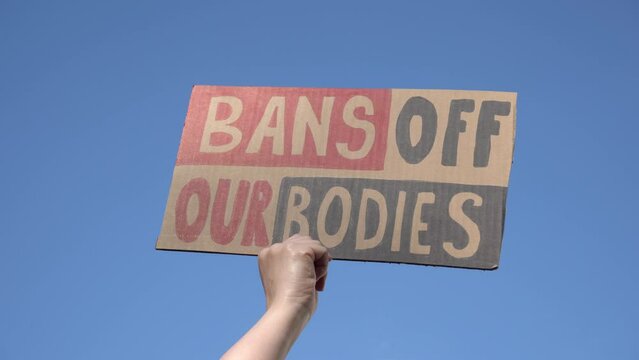 Woman hand holding placard sign with slogan Bans Off Our Bodies during manifestation. Female protester with banner supporting abortion rights at protest rally demonstration.